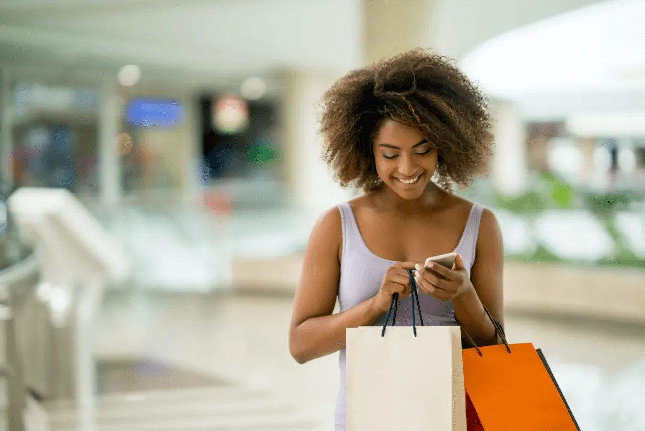 Image of woman with shopping bags smiling at her phone